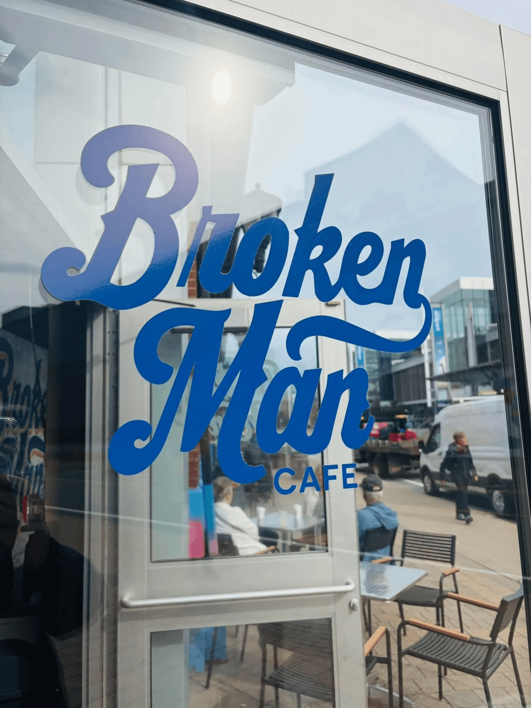 The window of a cafe. The sign says "Broken Man cafe," and you can see customers reflected in it.