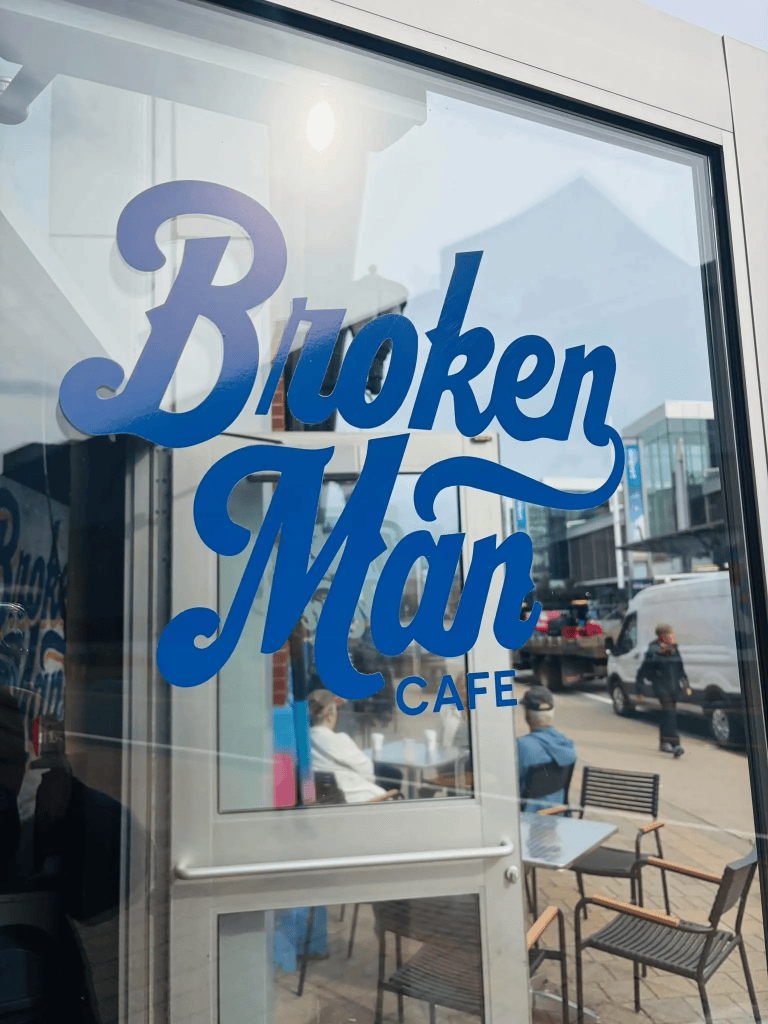 The window of a cafe. The sign says "Broken Man cafe," and you can see customers reflected in it.